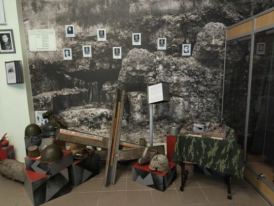 Каски, противотанковые ежи и стена с фотографиями в экспозиции музея